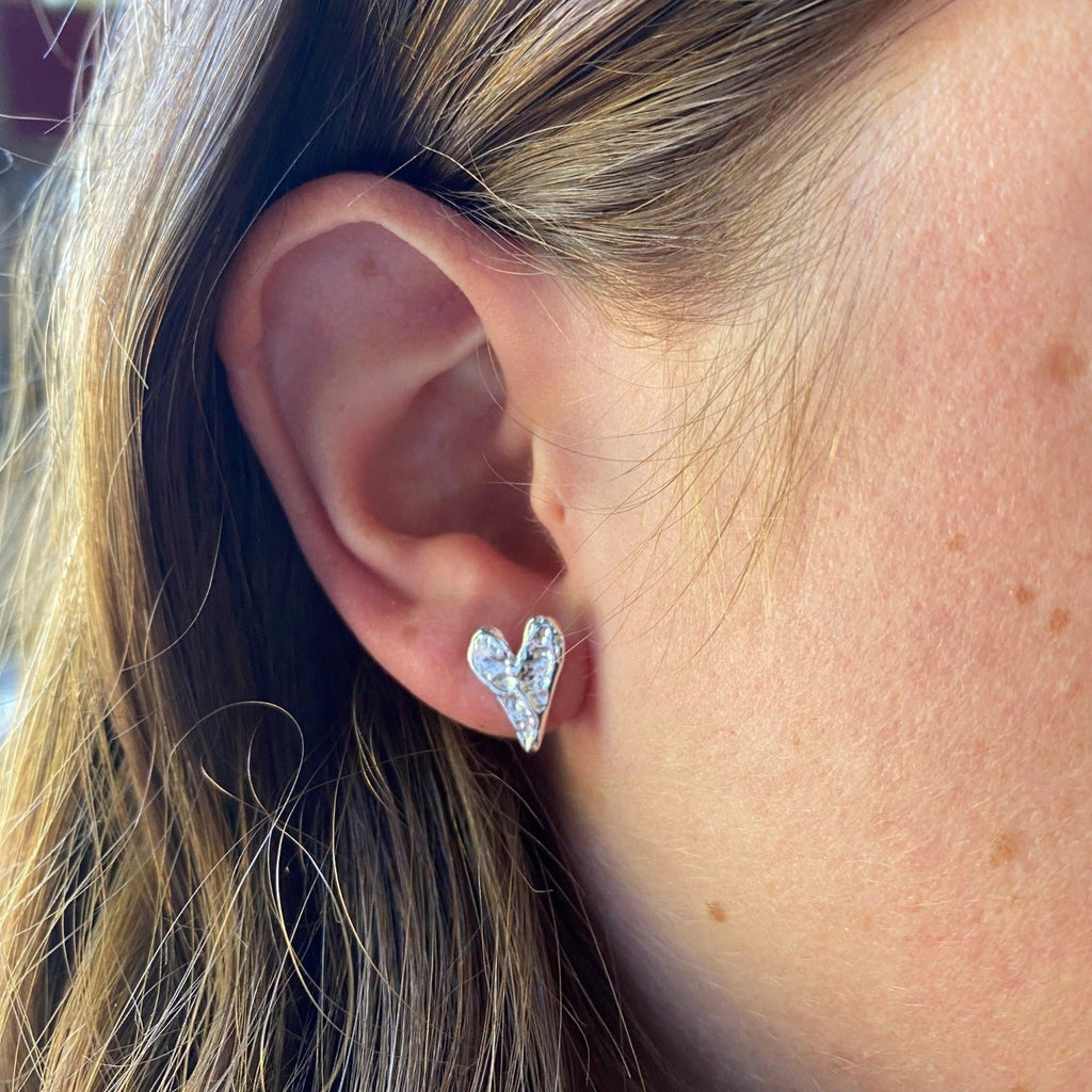 A sterling silver heart shaped stud earring with a textured finish, shown in a ladies ear.
