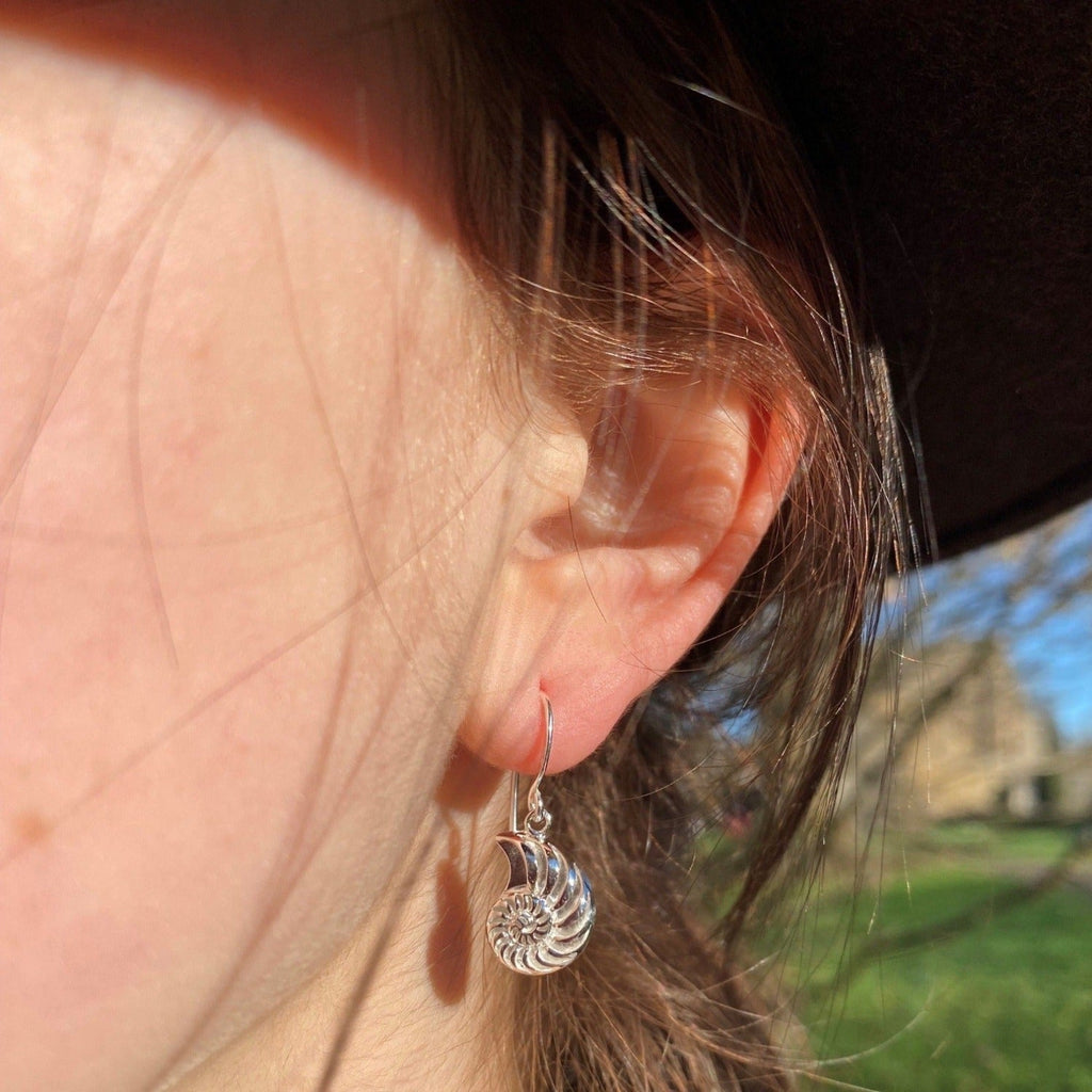 A pair of Sterling Silver Ammonite Drop Earrings, on silver hooks and shown in a ladies ear.