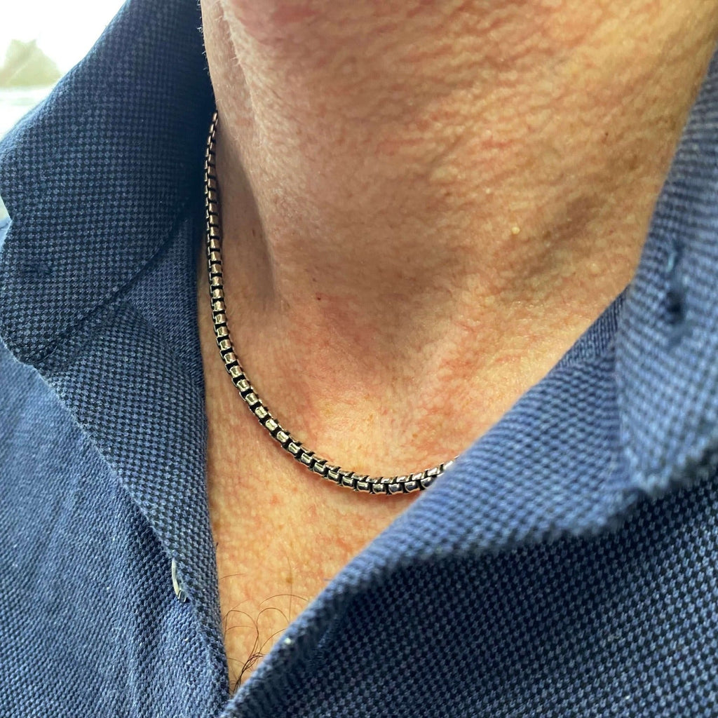 A sterling silver men's box chain, worn on a man's neck with an open shirt.
