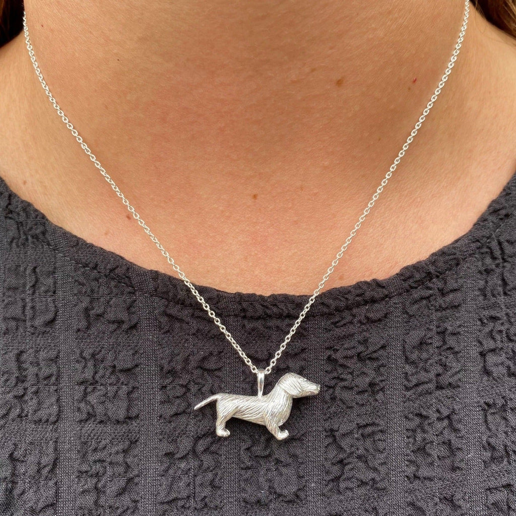 A sterling silver large dachshund necklace, hanging on a silver adjustable chain and worn on a model.