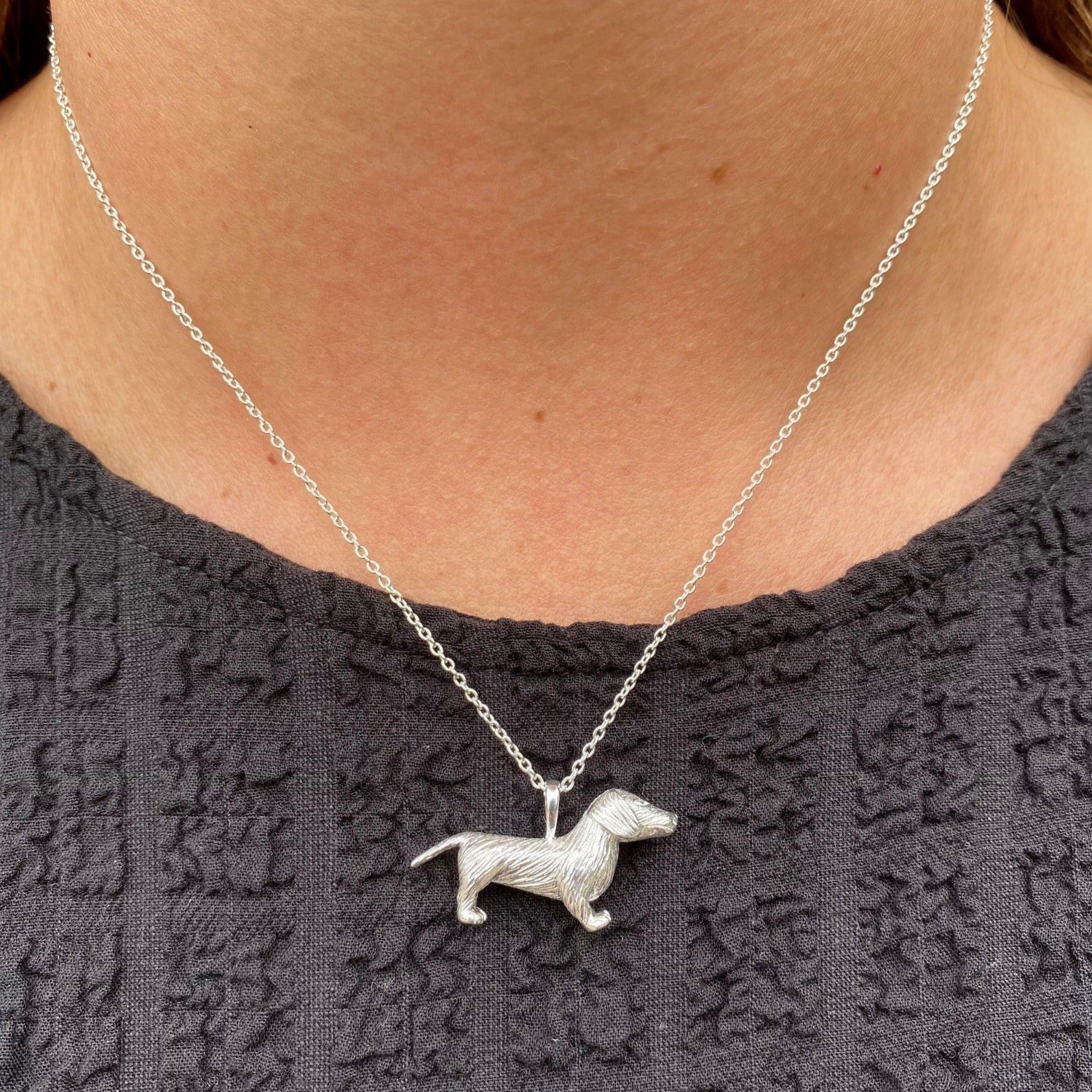 A sterling silver large dachshund necklace, hanging on a silver adjustable chain and worn on a model.