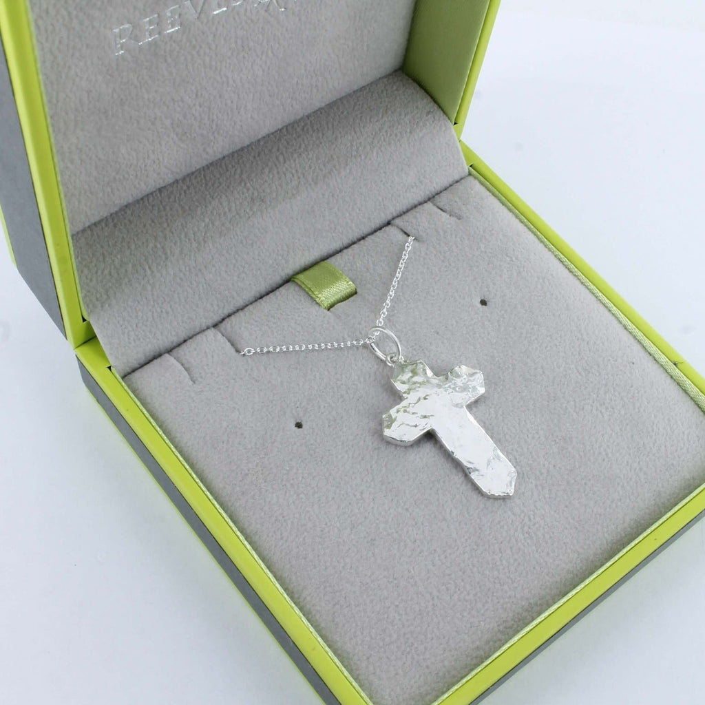 A sterling silver textured cross pendant with hammered detail, hung on a silver chain and shown in a Reeves & Reeves gift box.