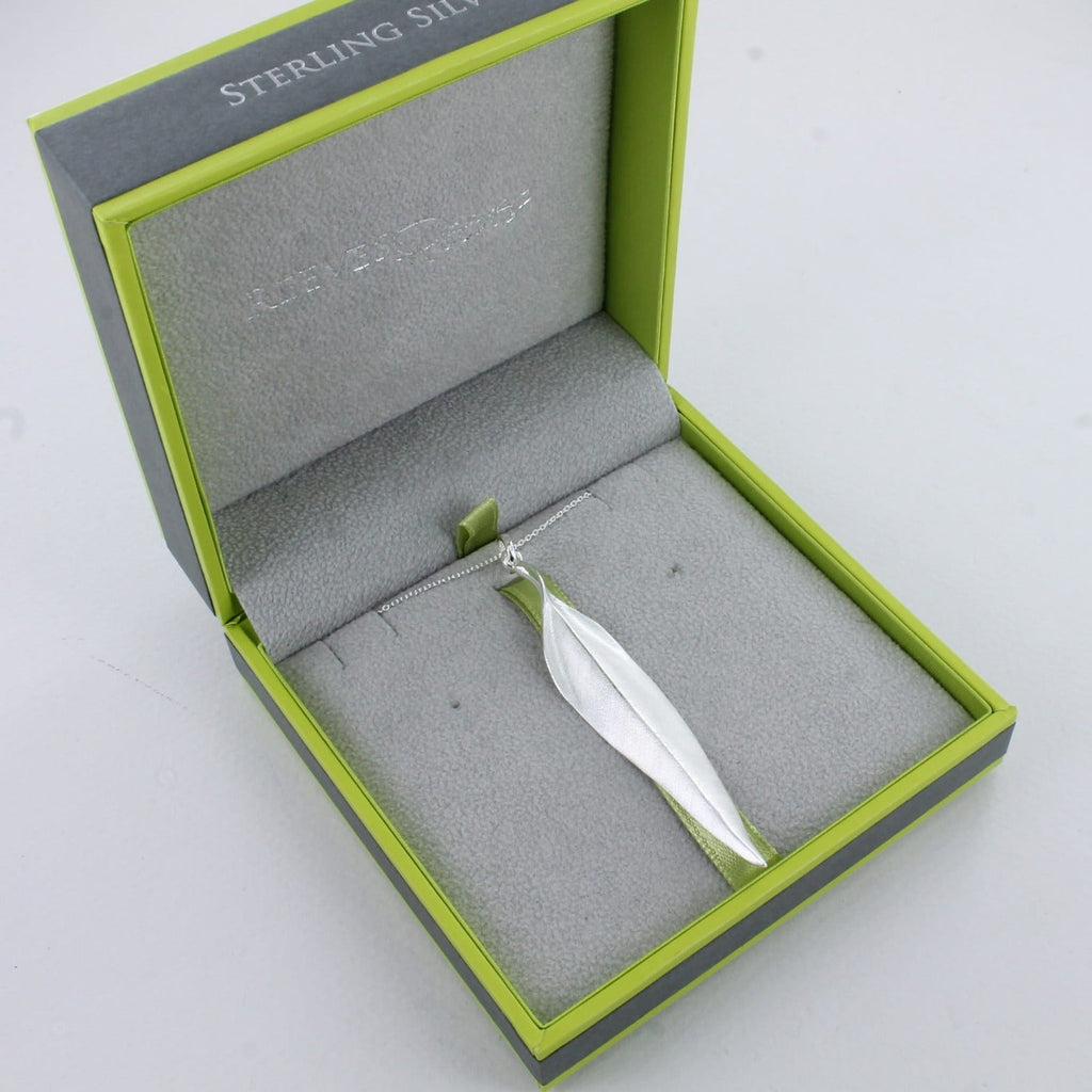 A Sterling Silver Leaf pendant which has a matt finish and gently curved edges. The leaf hangs on a silver chain and is shown in a grey and green Reeves & Reeves branded gift box.