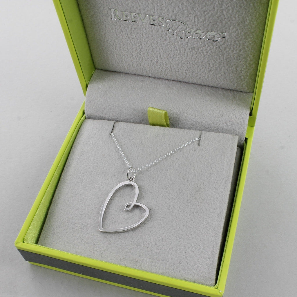 A silver heart pendant hanging on a sterling silver adjustable chain. Shown in a Reeves & Reeves branded box.