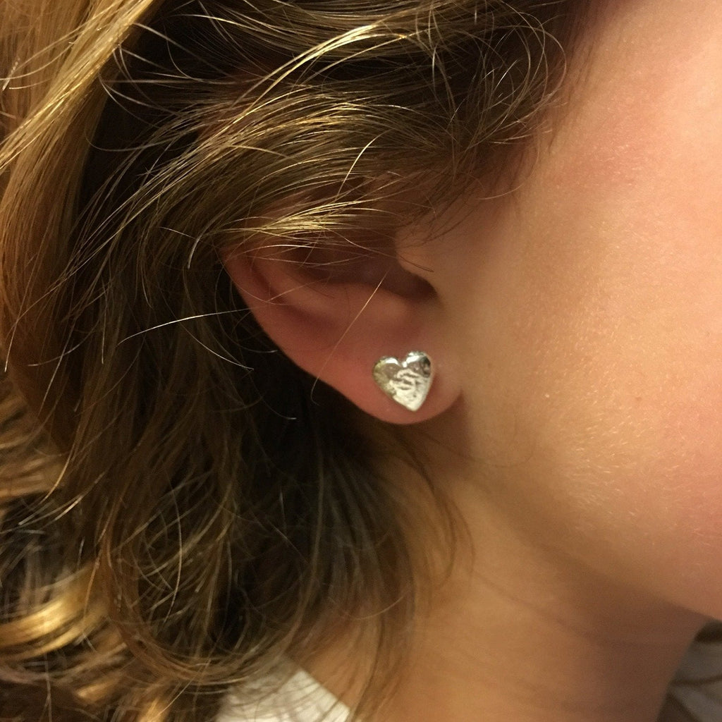A heart stud earring in sterling silver, shown in a ladies ear.