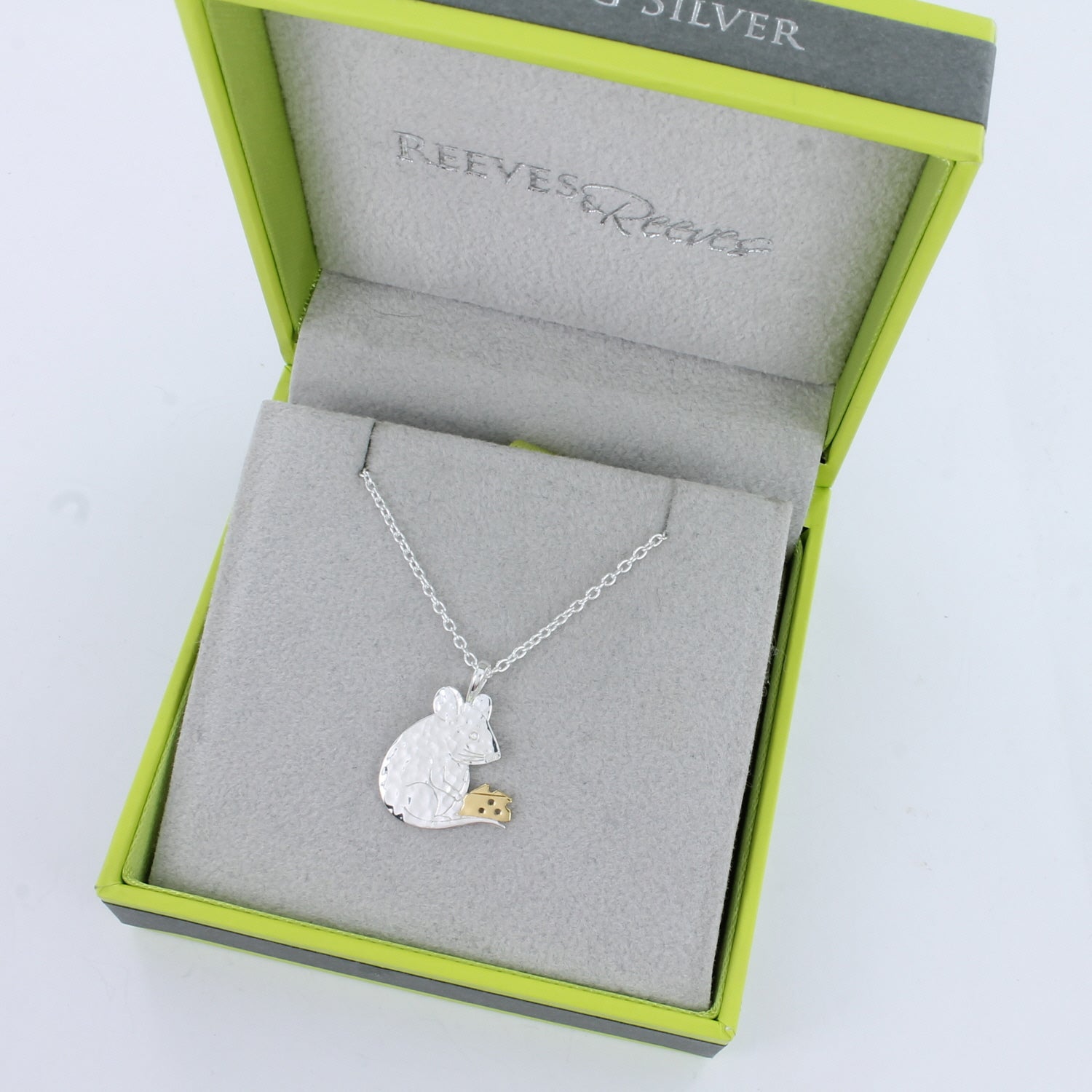 A Sterling Silver flat Mouse holding a gold plated block of cheese and hung on a silver chain. Shown in a Reeves & Reeves grey and green branded gift box.