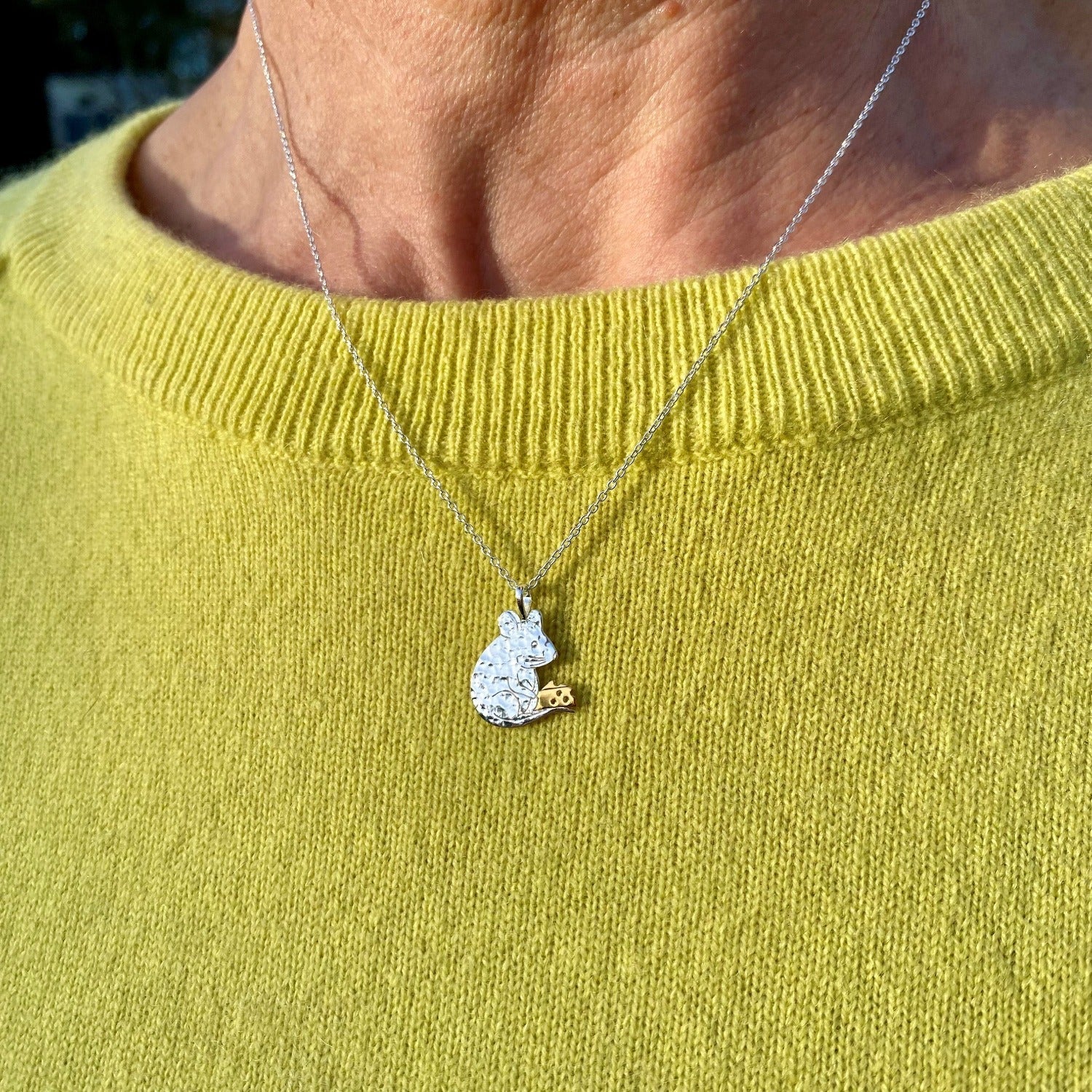 A Silver flat mouse pendant, holding a gold plated block of cheese and hung on a silver adjustable chain.