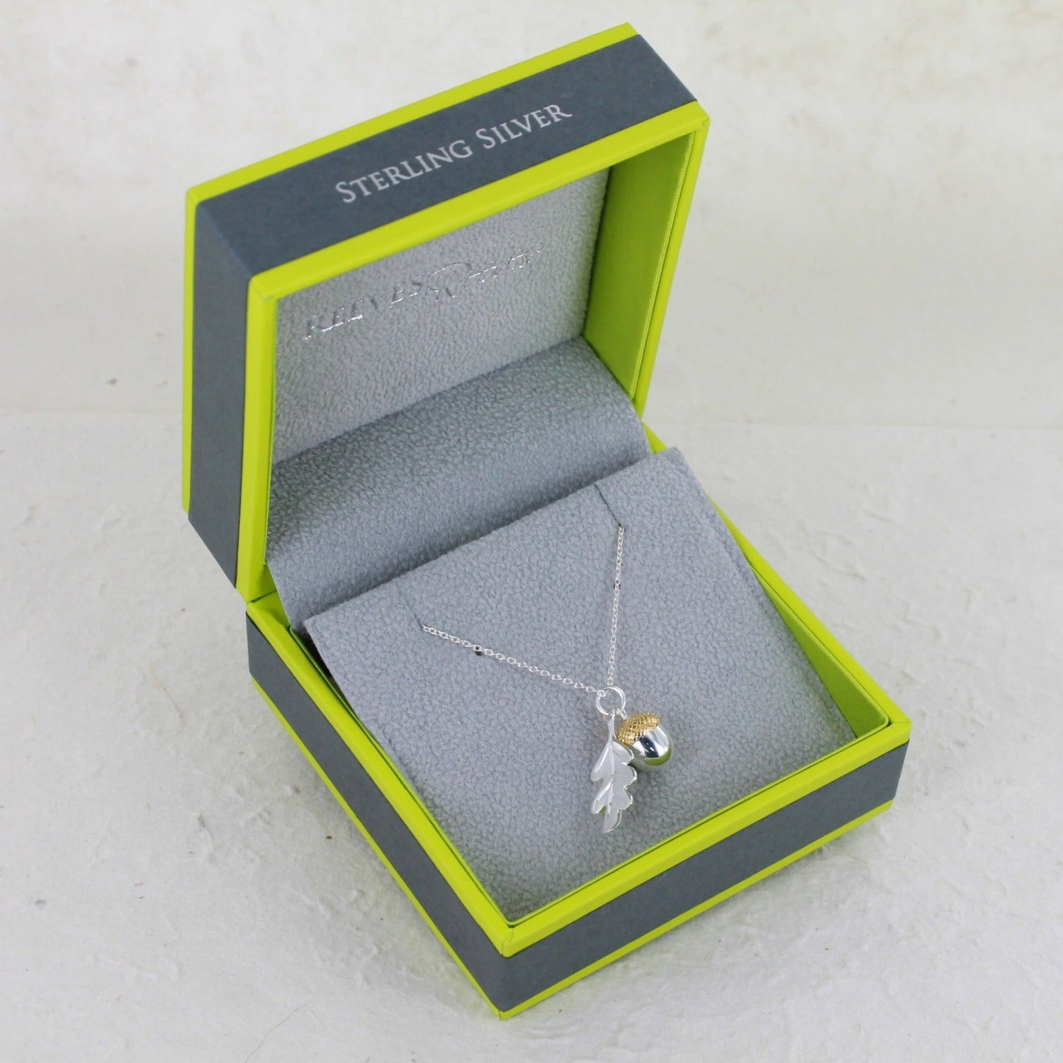 Silver and Gold Plate Acorn and Oak Leaf Pendant hanging on a silver adjustable chain, shown in a Reeves & Reeves branded grey and green box.