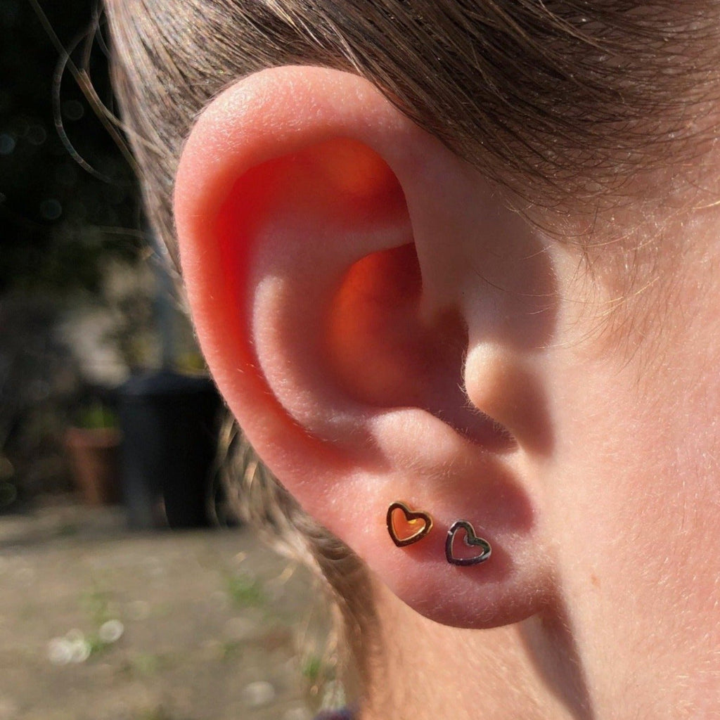 Two heart silhouette stud earrings, one silver and one 18ct gold plate, shown in a ladies ear.