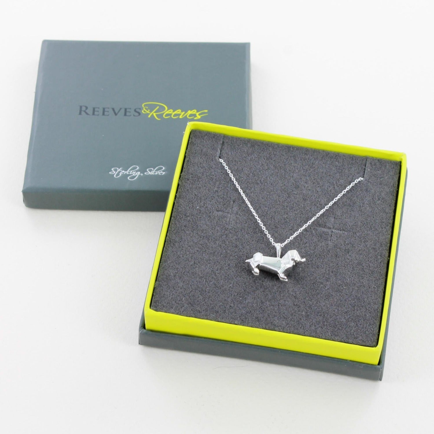 Sterling Silver Dachshund Pendant with an origami design and hanging on a silver adjustable chain and in a Reeves & Reeves grey and green branded gift box.