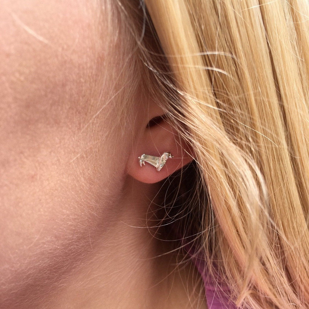 A sterling silver Dachshund Stud Earrings in an origami design, shown in a ladies ear.