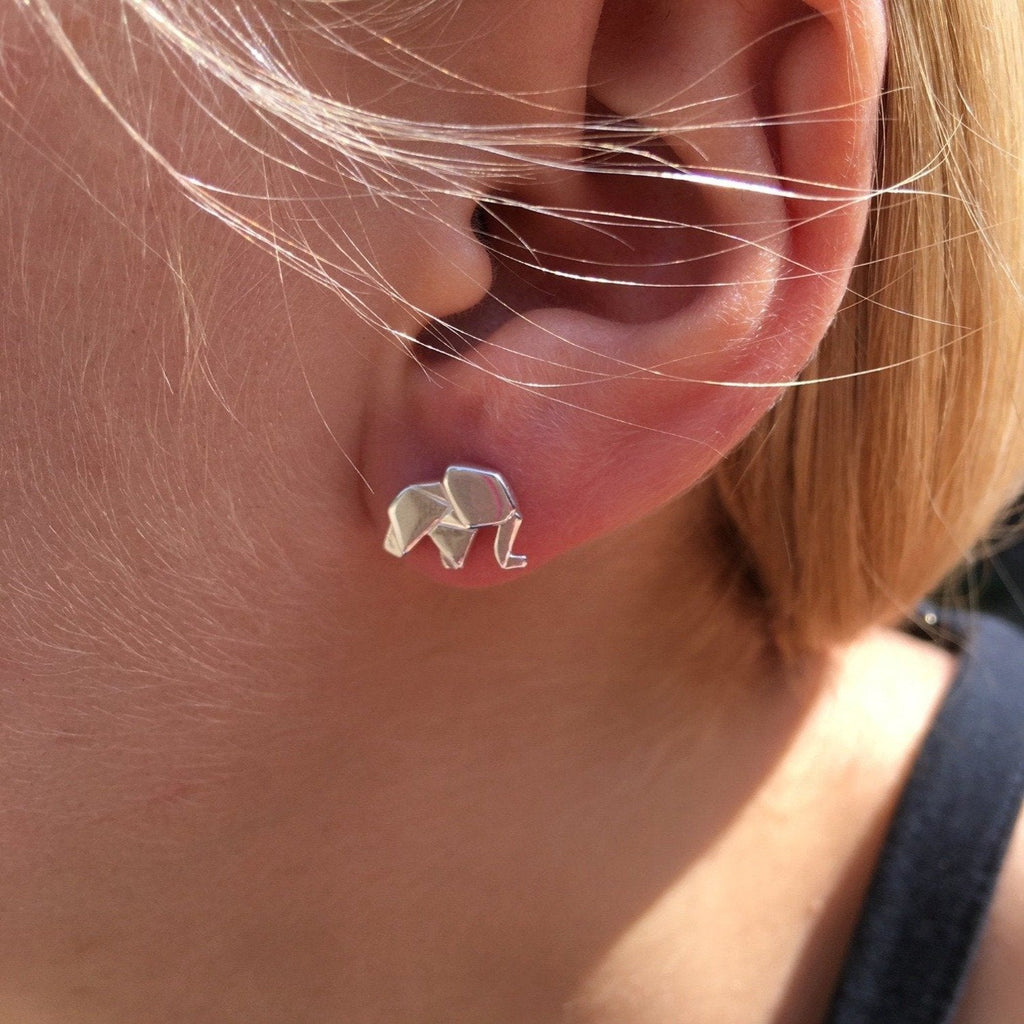 A sterling silver elephant stud earring in an origami style, and worn in a ladies ear.