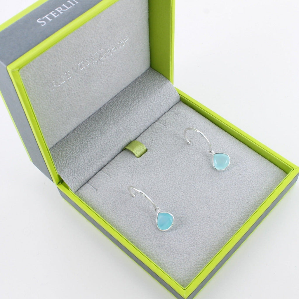 A pair of sterling silver hoop earrings with a pear shaped aqua chalcedony stone hanging from the bottom and shown in a Reeves & Reeves gift box.