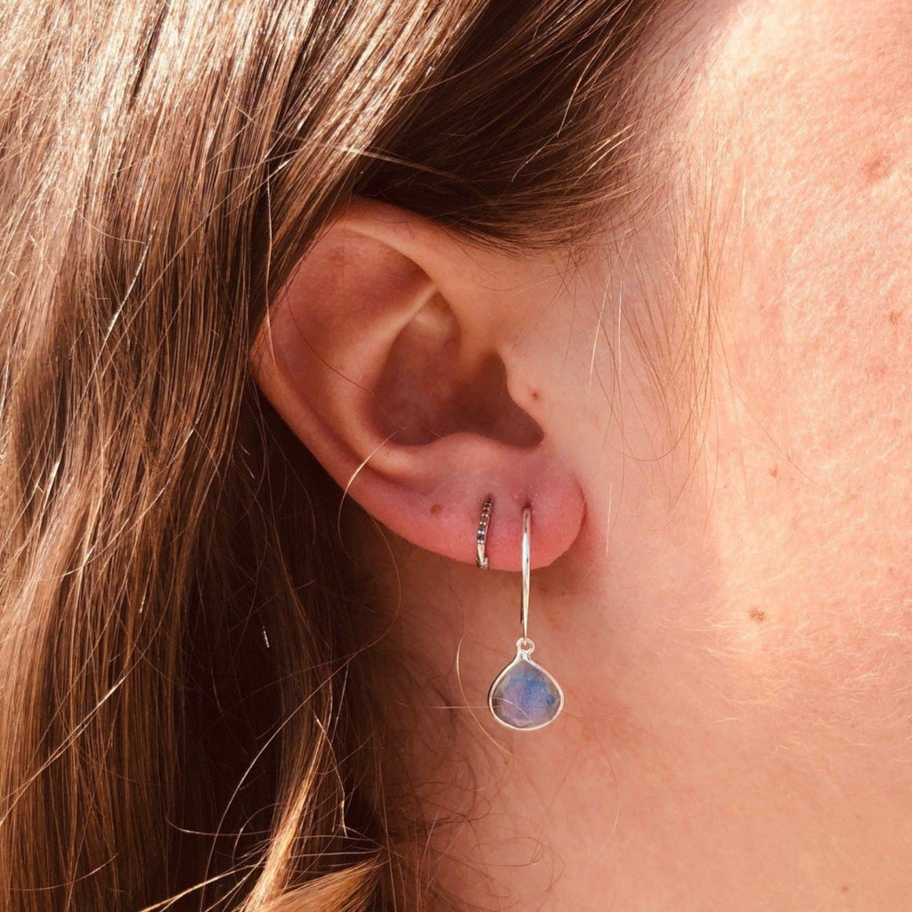 A sterling silver hoop style earring with a labradorite pear shaped stone hanging from the bottom. Worn in a ladies ear.