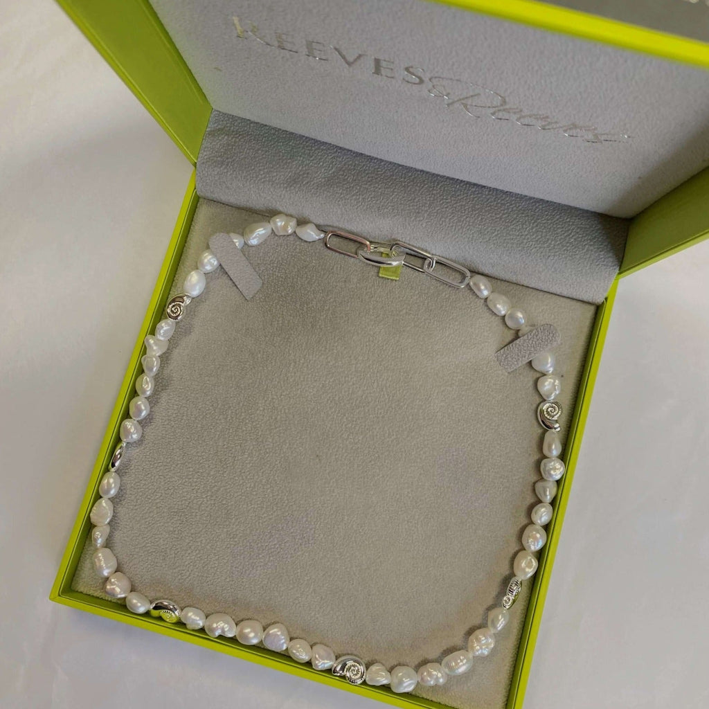 A sterling silver necklace with freshwater pearls all along the chain and interspersed with silver ammonites. Shown in a Reeves & Reeves gift box.