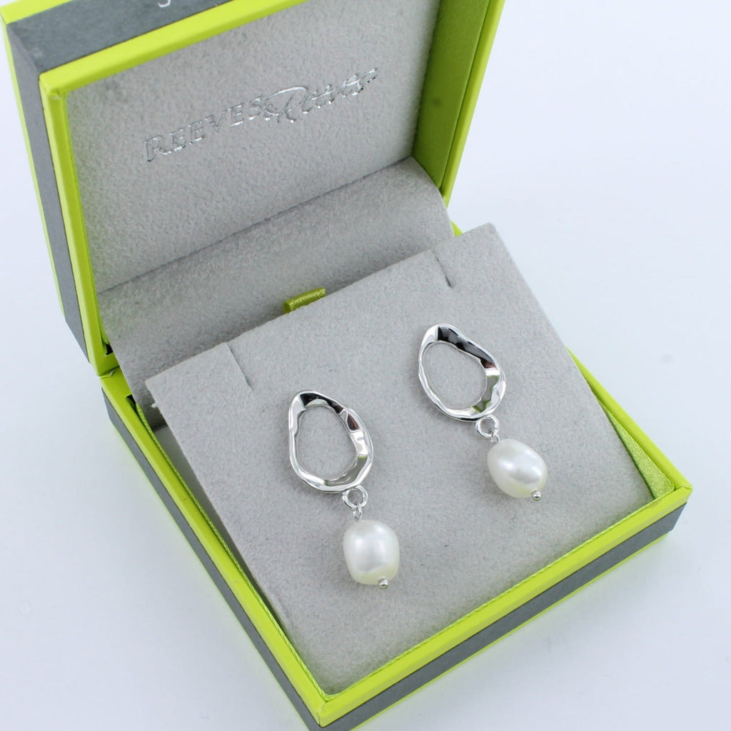 A pair of sterling silver ringlet style stud earrings with a white freshwater pearl hanging from the bottom. Shown in a Reeves & Reeves gift box.