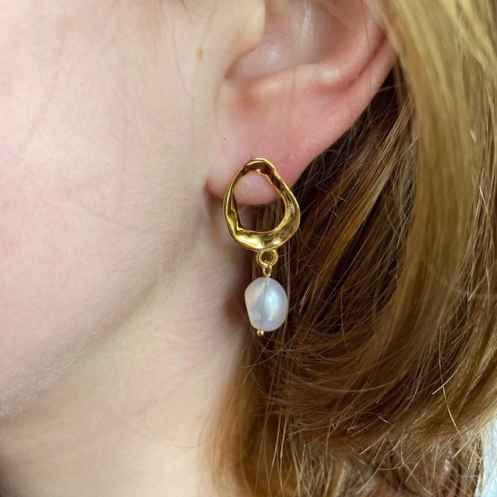 A ringlet style stud earring in silver and with 18ct gold plate. The earrings have a white freshwater pearl hanging from the bottom and are shown in a ladies ear.