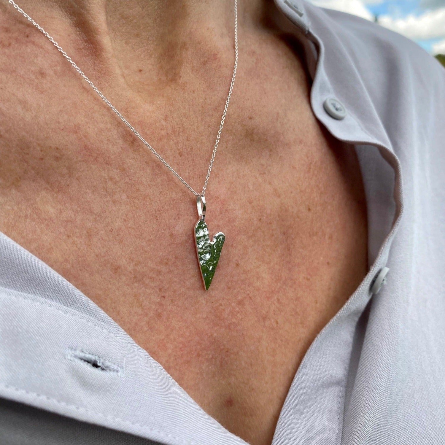 A silver heart pendant, worn on an adjustable silver chain and shown on a women's neck.