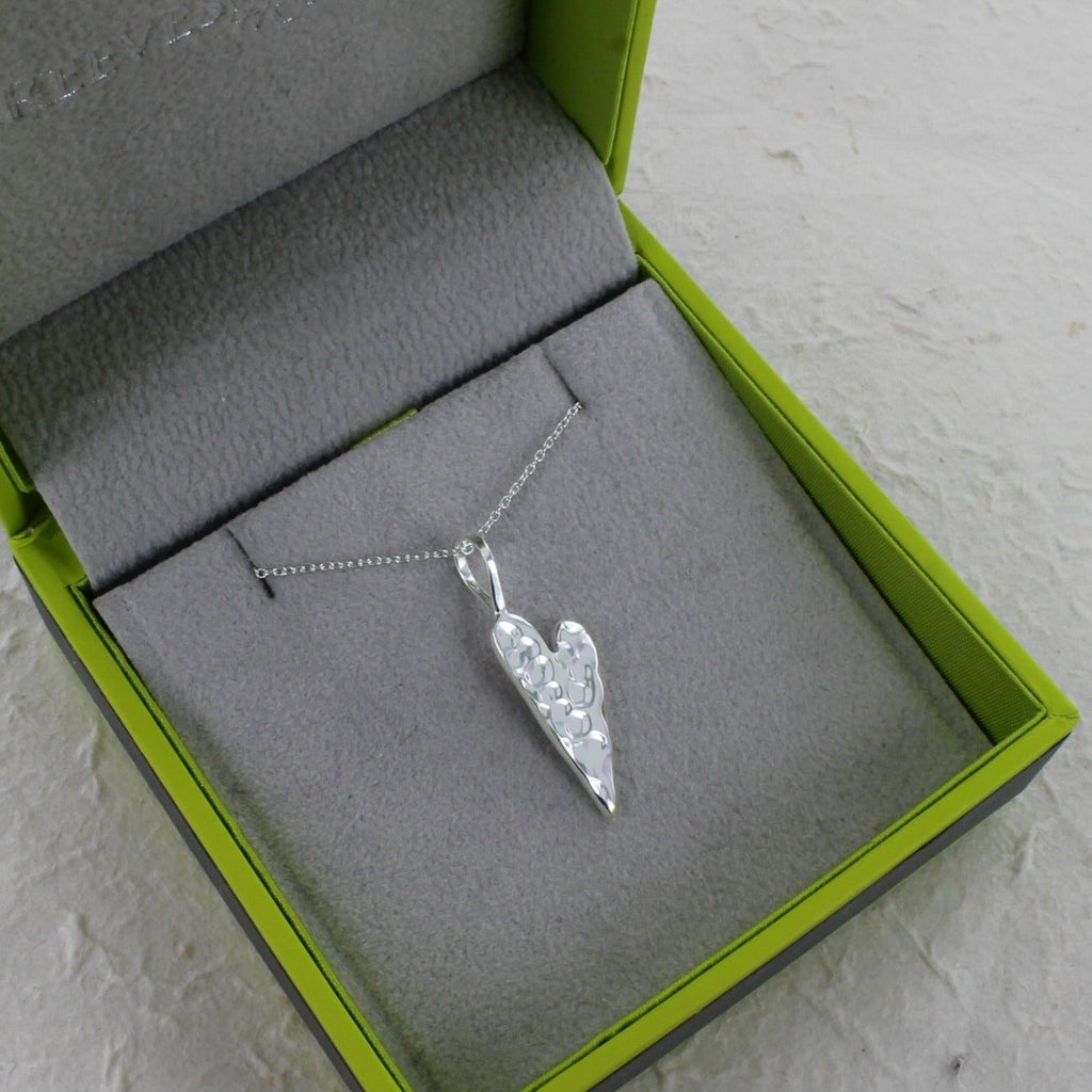 A silver textured heart pendant on an adjustable silver chain and shown in a Reeves & Reeves grey and green gift box.