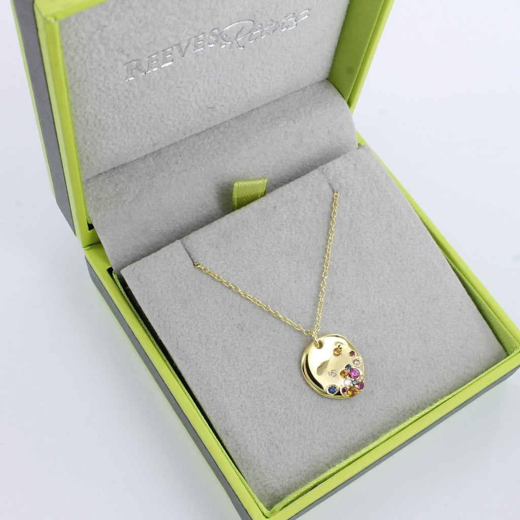 A rainbow stone pebble necklace in gold plate, with multi coloured stones , hanging on a gold chain and shown in a Reeves & Reeves branded gift box.