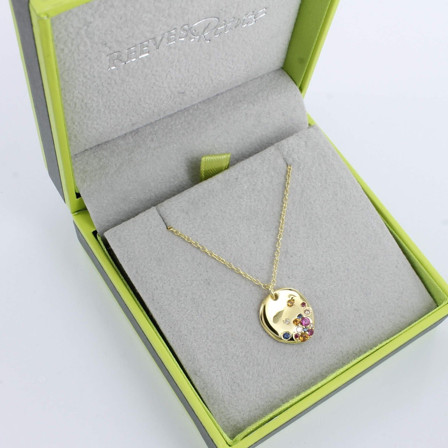 A rainbow stone pebble necklace in gold plate, with multi coloured stones , hanging on a gold chain and shown in a Reeves & Reeves branded gift box.