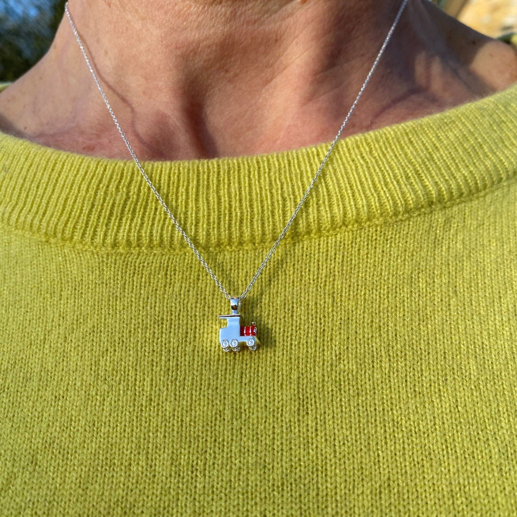 A sterling silver train necklace with red enamel detail, hung on a silver chain and worn on a ladies neck over a jumper.