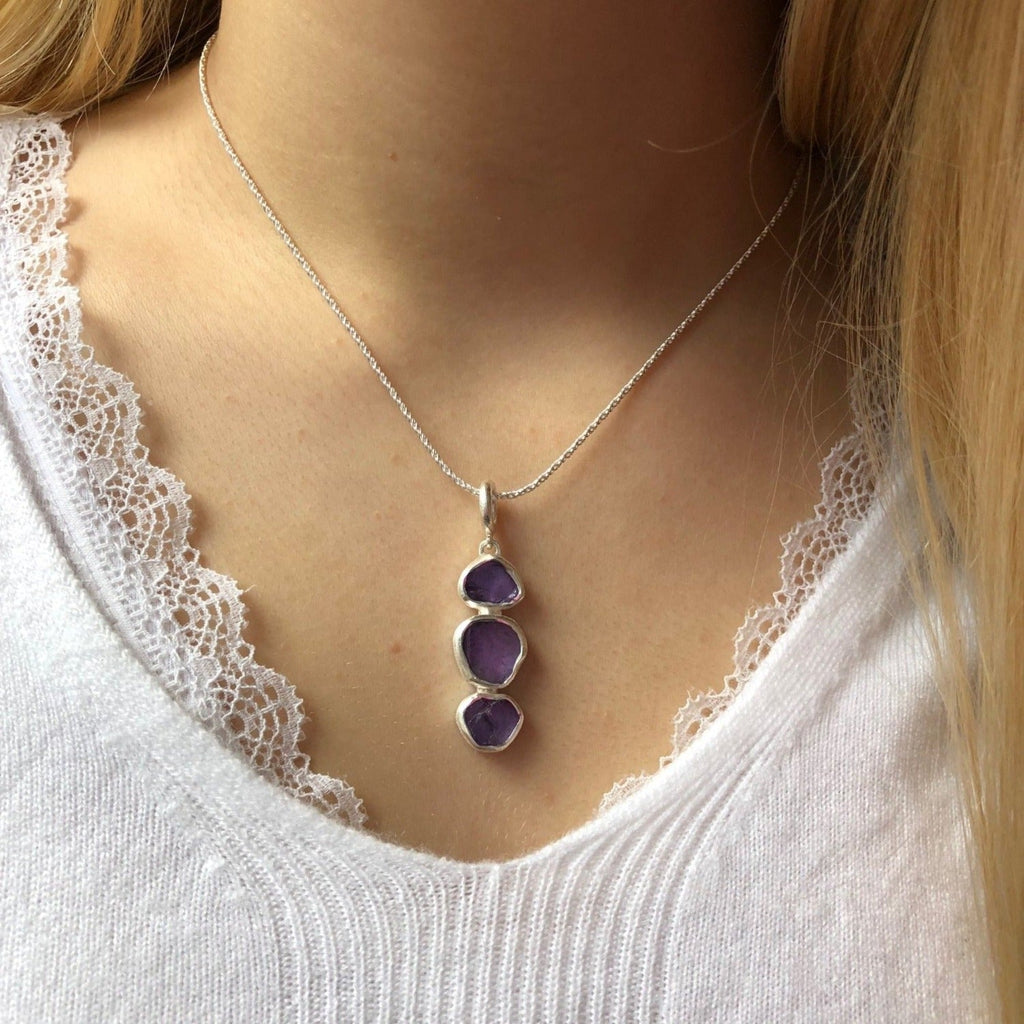 Three rough amethyst stones, set in silver and hung vertically from a silver rope style chain.
