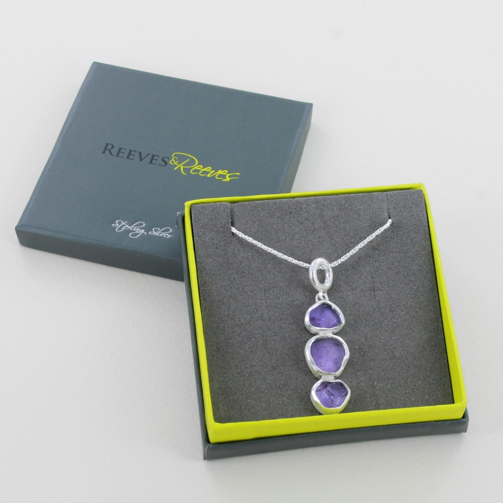 Three rough cut amethyst stones, hung vertically from a silver rope chain. Shown in a Reeves & Reeves grey and green branded gift box.