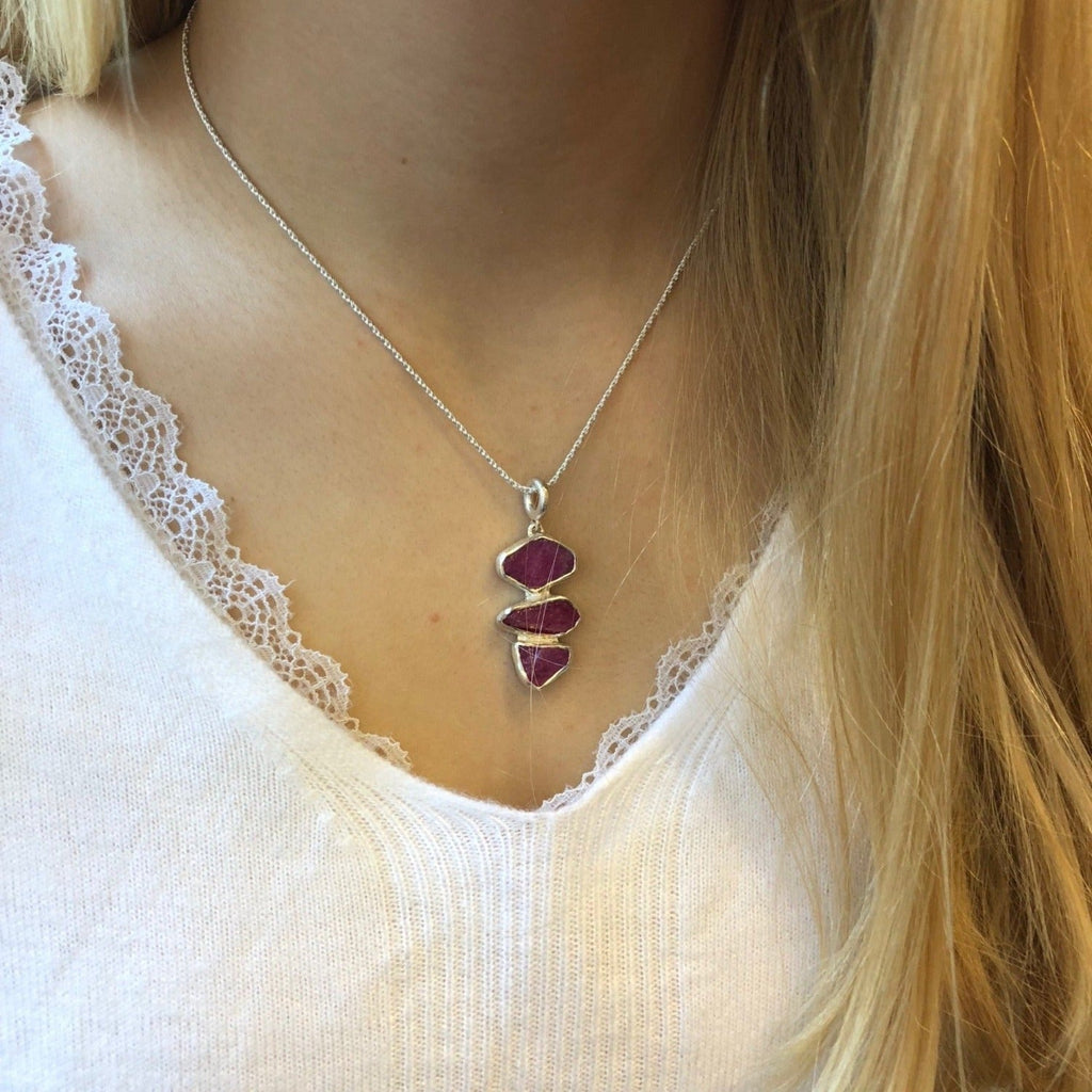 A sterling silver pendant with rough cut ruby stones set in silver in a vertical design, hung on a silver adjustable chain and worn on a model.