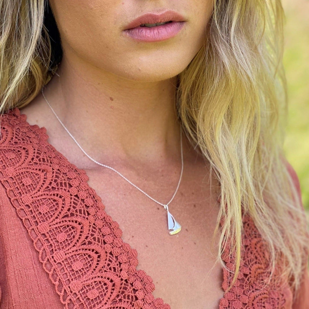 Silver sailboat pendant hanging on a silver chain and worn on a model.