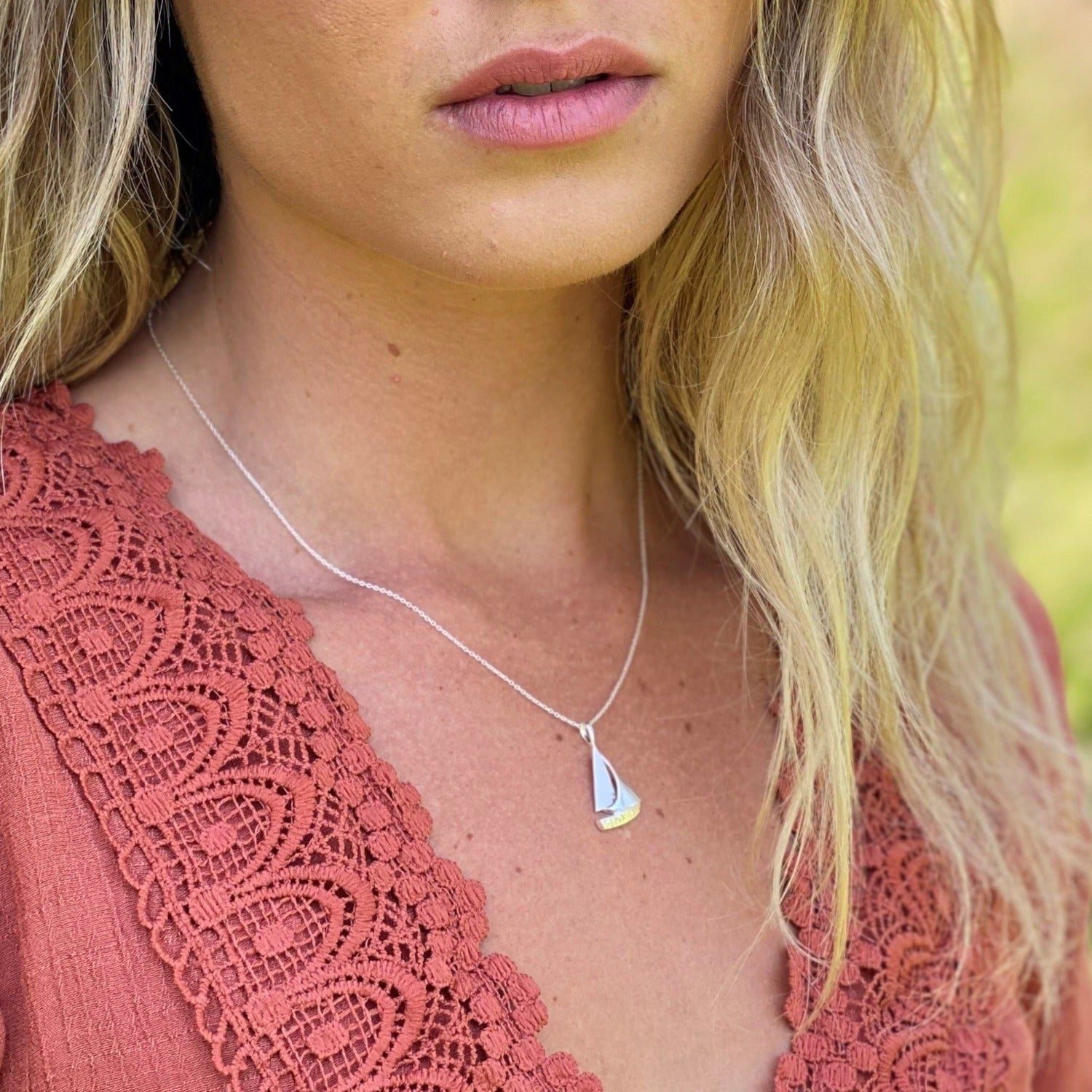 Silver sailboat pendant hanging on a silver chain and worn on a model.