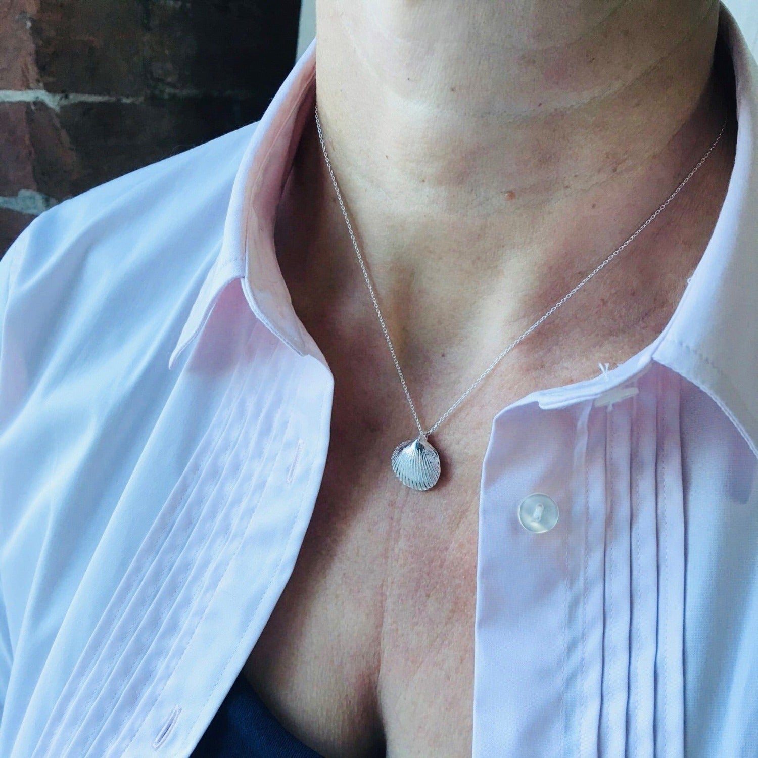 A scalloped shell pendant hanging on a silver adjustable chain and worn on a model.