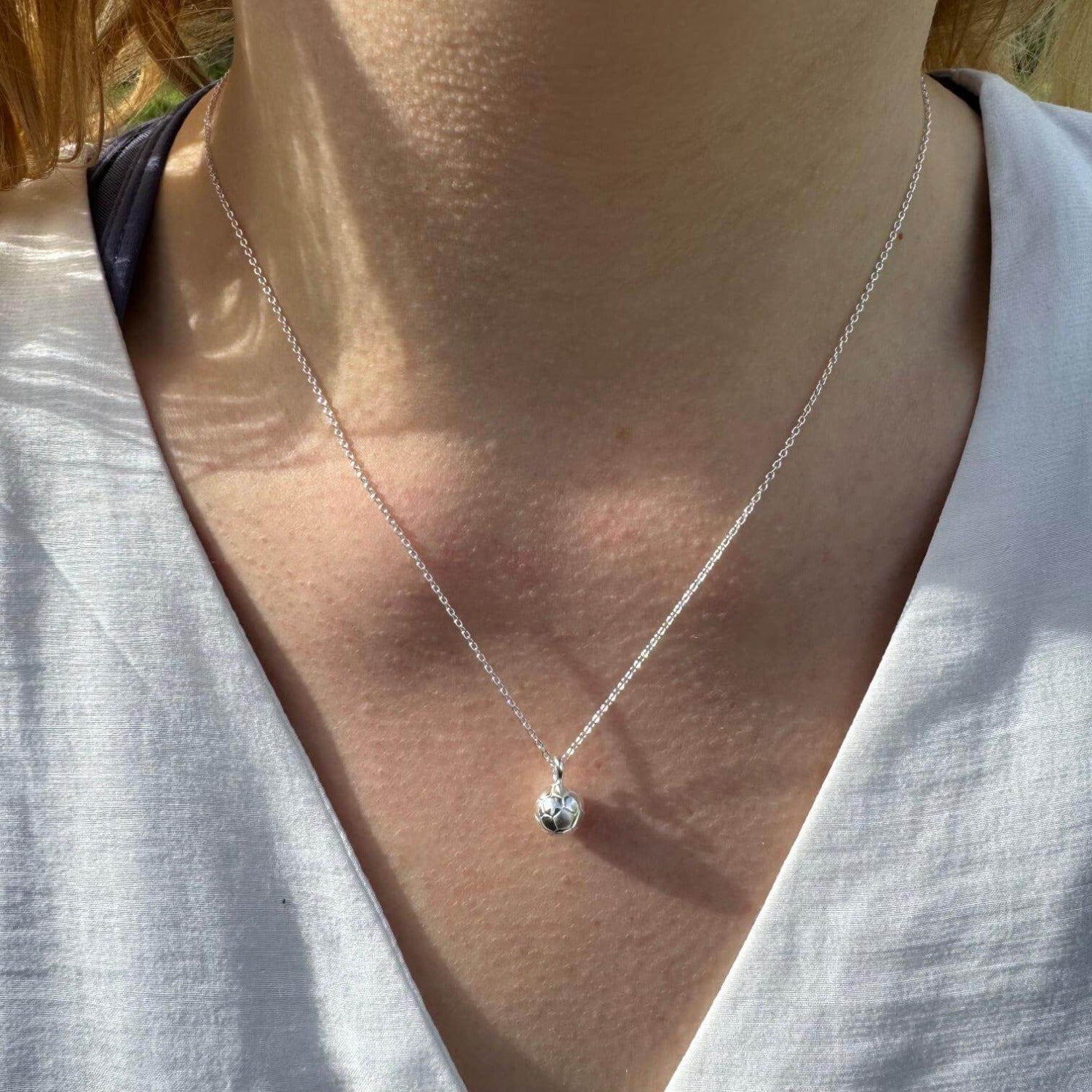 A sterling silver football pendant, shown on a silver adjustable chain and worn on a models neck.