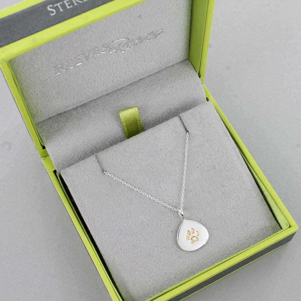 A silver teardrop pendant with a gold plated pawprint design in the centre. Hangs on a silver adjustable chain and shown in a Reeves & Reeves gift box.