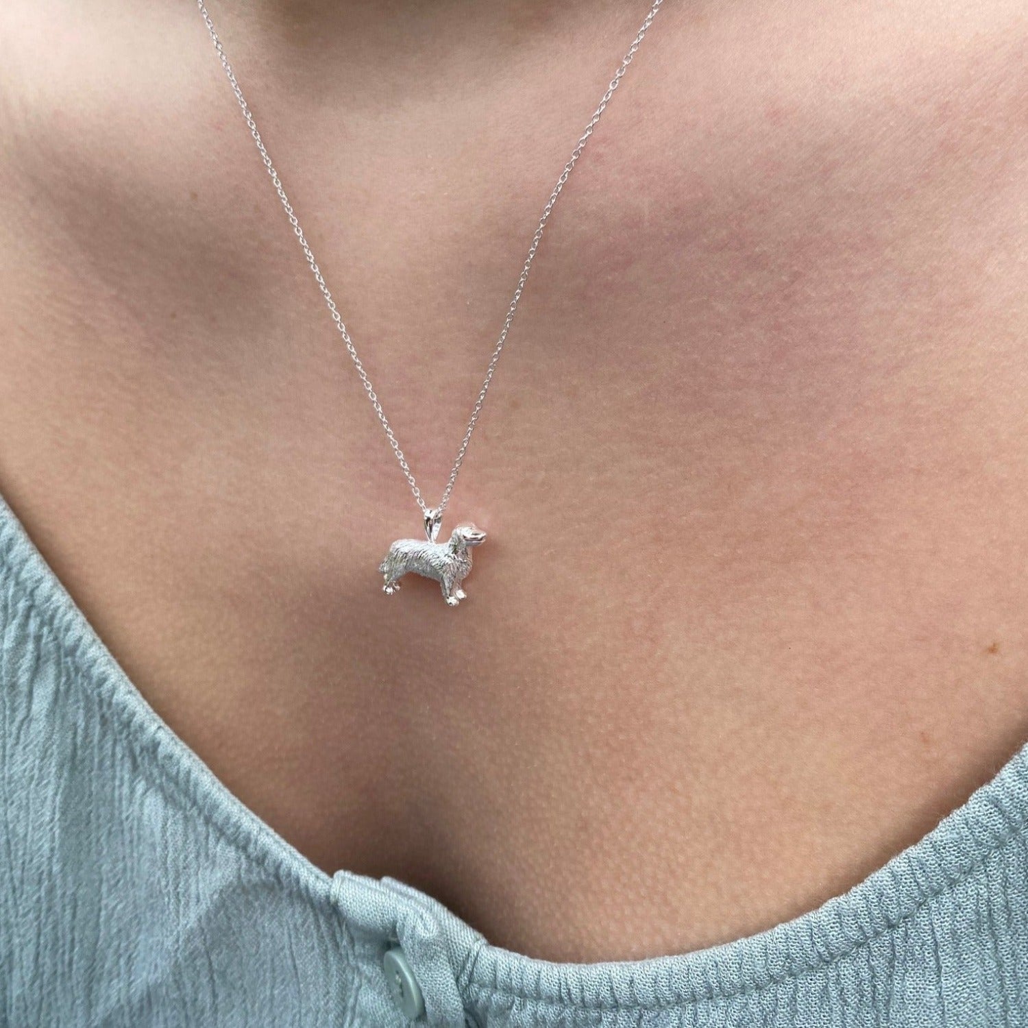 A Sterling Silver Retriever pendant, hung on a silver chain and worn on a models neck.