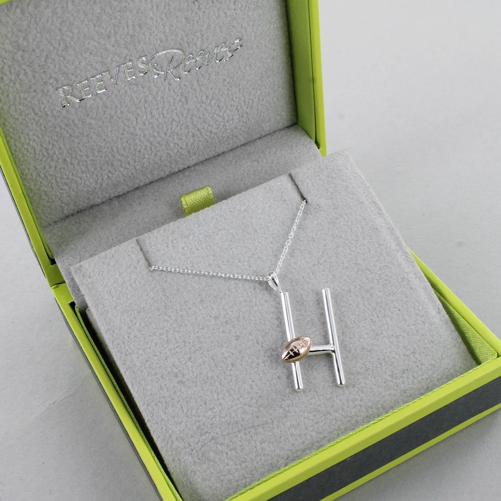 A Sterling Silver Rugby pendant with a rose gold plated rugby ball sat on the posts. Hung on a silver adjustable chain and shown in a Reeves & Reeves grey and green branded gift box.