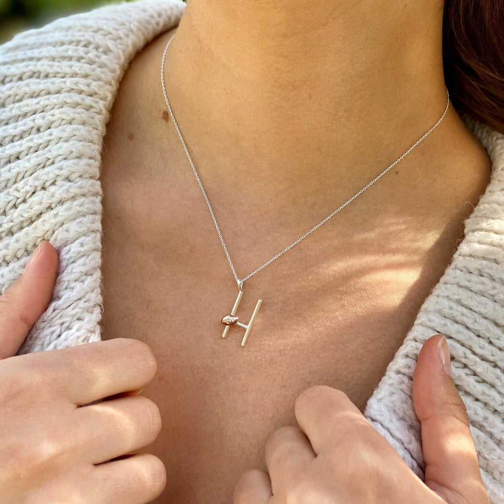  A Sterling Silver Rugby post Necklace with a rose gold plated rugby ball sat on the posts. Hung on a silver adjustable chain and worn on a models neck.