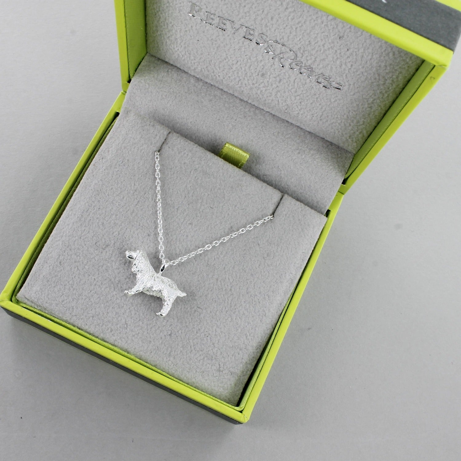 A silver Spaniel Necklace on a silver chain and shown in a Reeves & Reeves grey and green branded gift box.