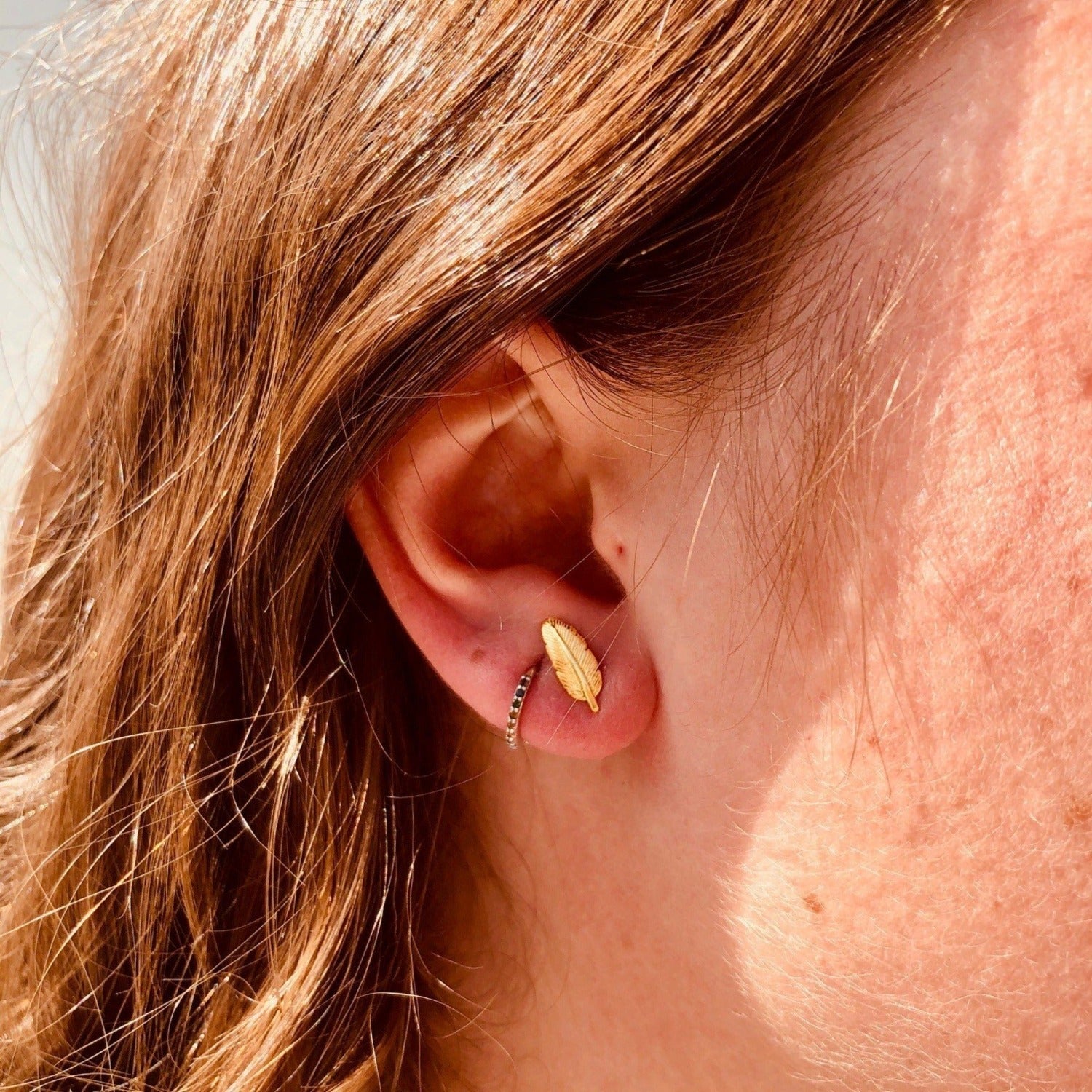 A sterling silver feather stud with 18ct gold plating, shown in a ladies ear.