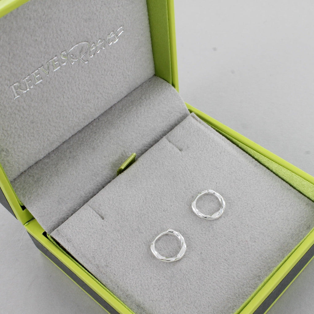 A pair of sterling silver huggies with a twist style, shown in a Reeves & Reeves gift box.