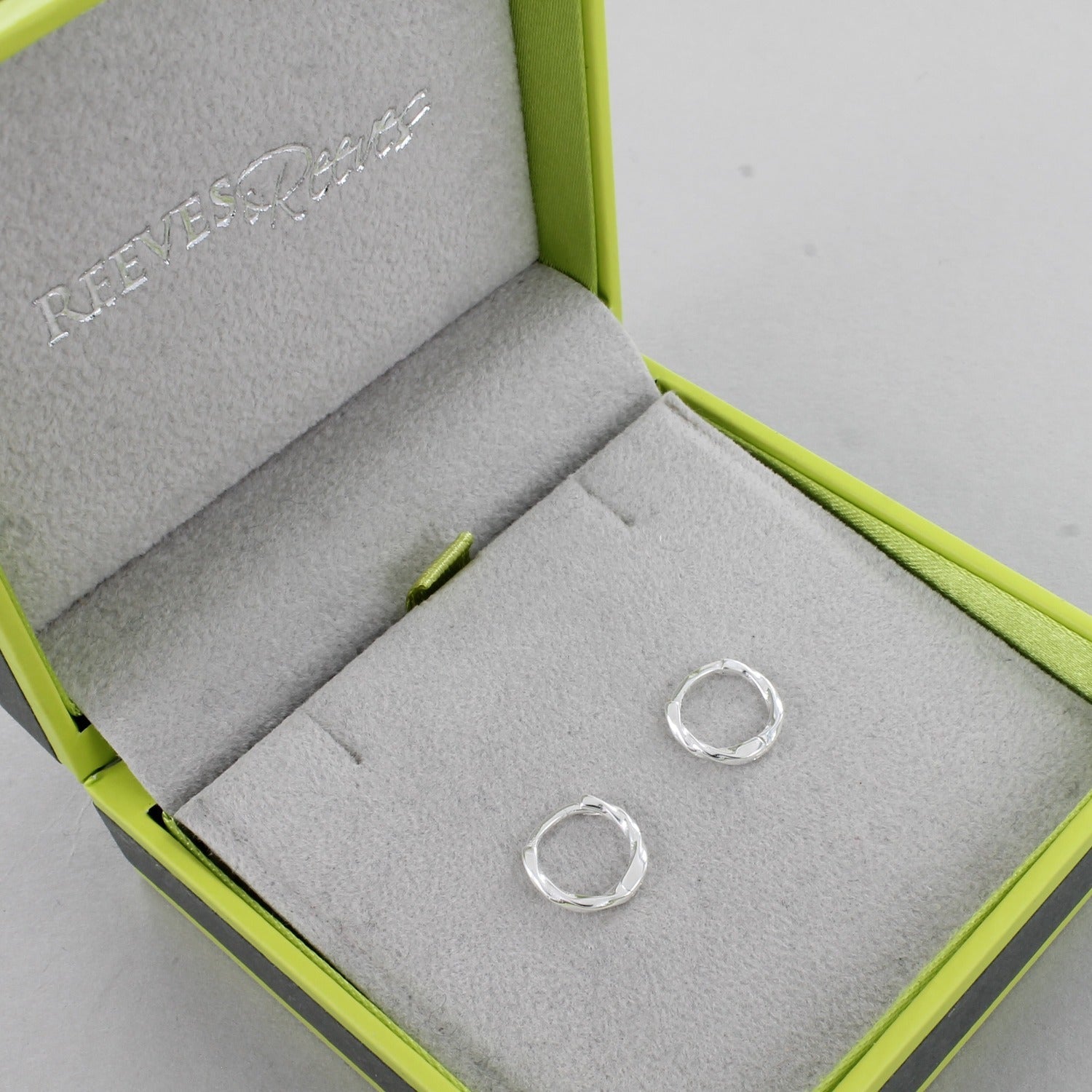 A pair of sterling silver huggies with a twist style, shown in a Reeves & Reeves gift box.