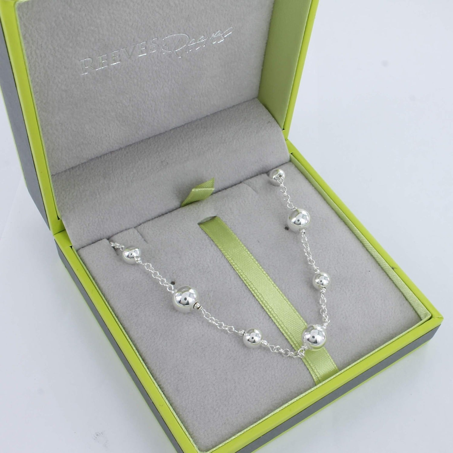 A silver beaded chain necklace, with varying bead sizes spread evenly along the chain. Shown in a Reeves & Reeves grey and green branded gift box.