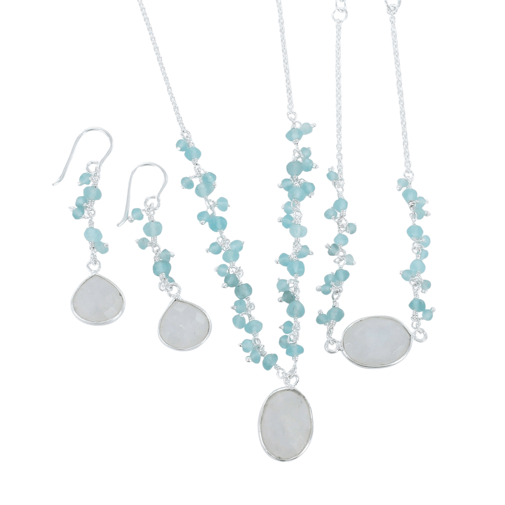 A silver chain necklace with an oval shaped moonstone hanging from the centre of the chain. Small Aqua chalcedony stones sit in clusters up either side of the chain. Shown with the matching bracelet and drop earrings.