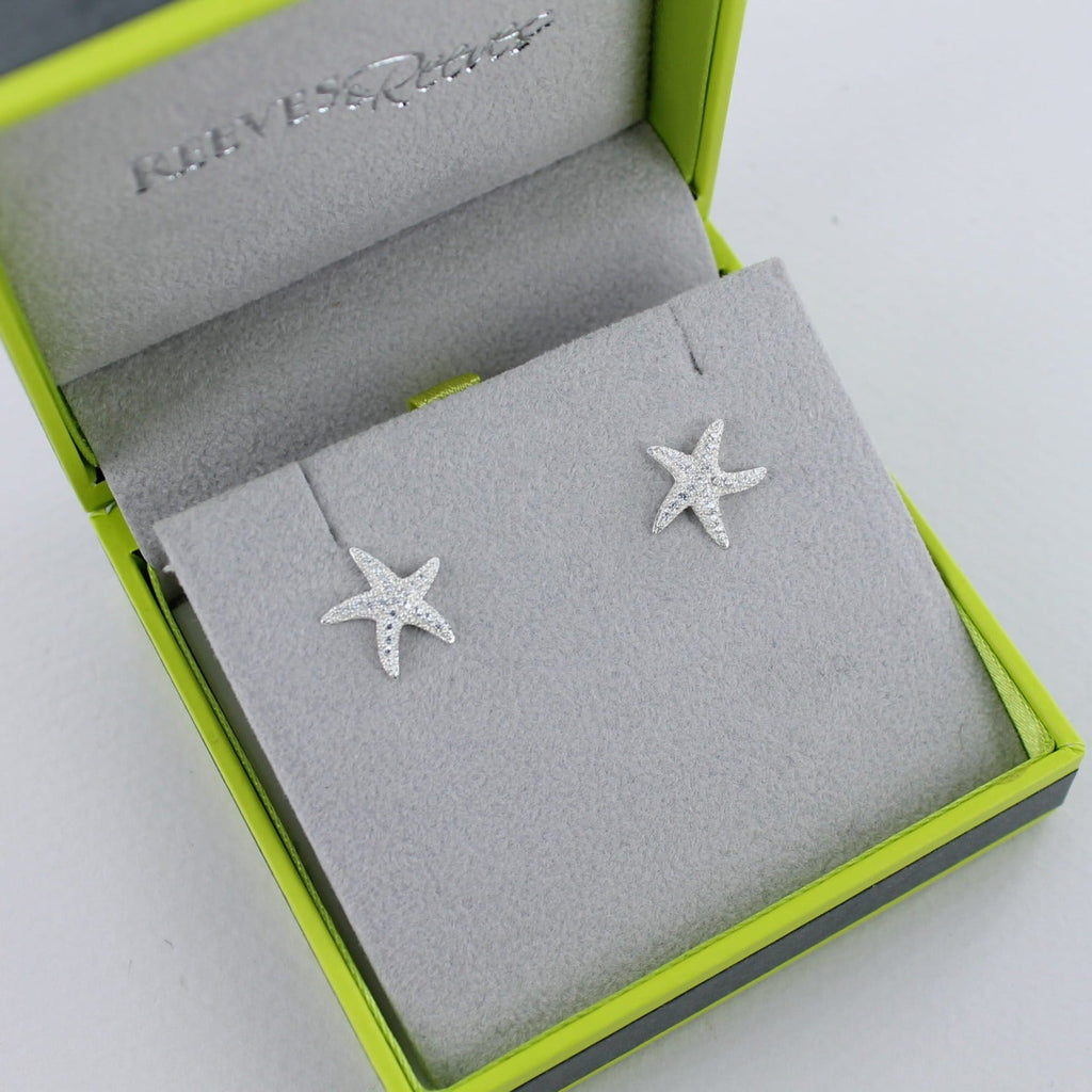 A pair of sterling silver starfish stud earrings with cubic zirconia stones, shown in a Reeves & Reeves gift box.