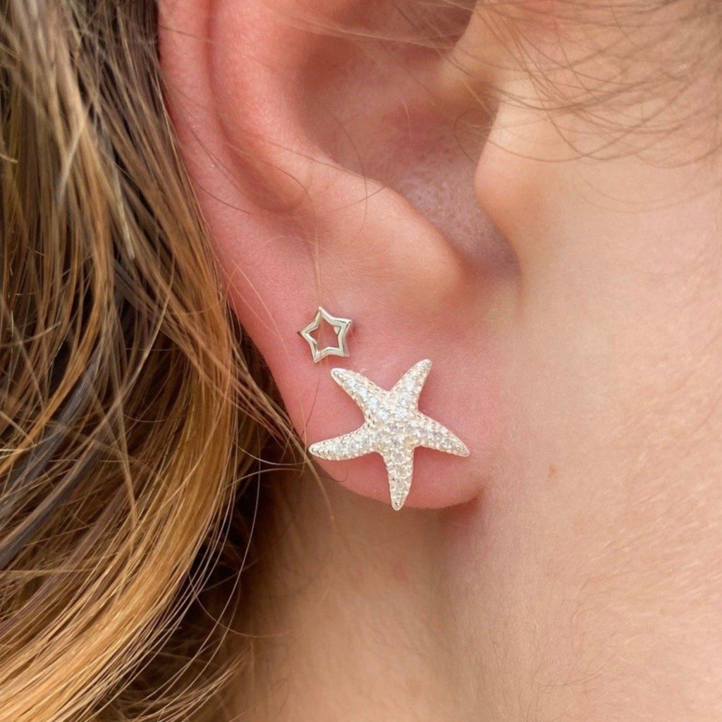 A sterling silver starfish stud earring, filled with cubic zirconia stones and shown in a ladies ear.