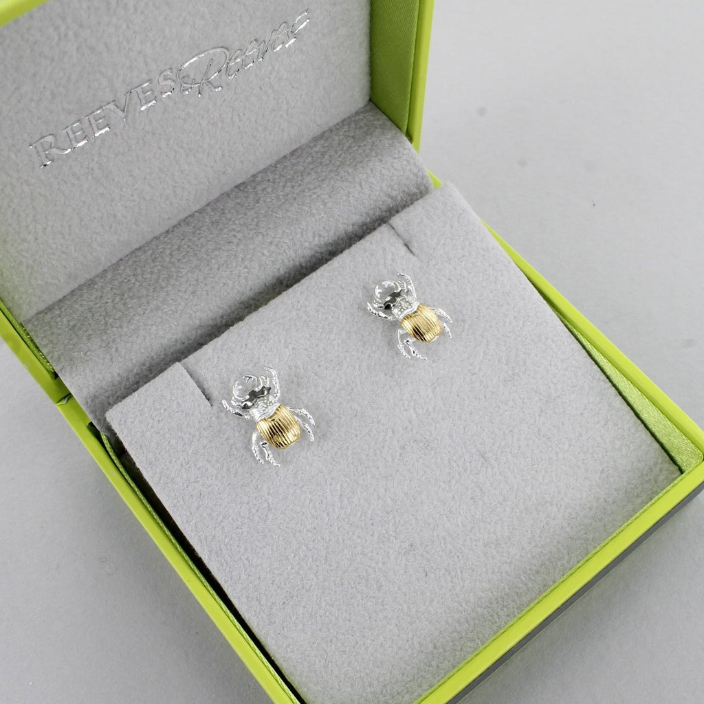 A pair of stag beetle stud earrings in silver with gold plated finish and shown in a Reeves & Reeves grey and green branded gift box.