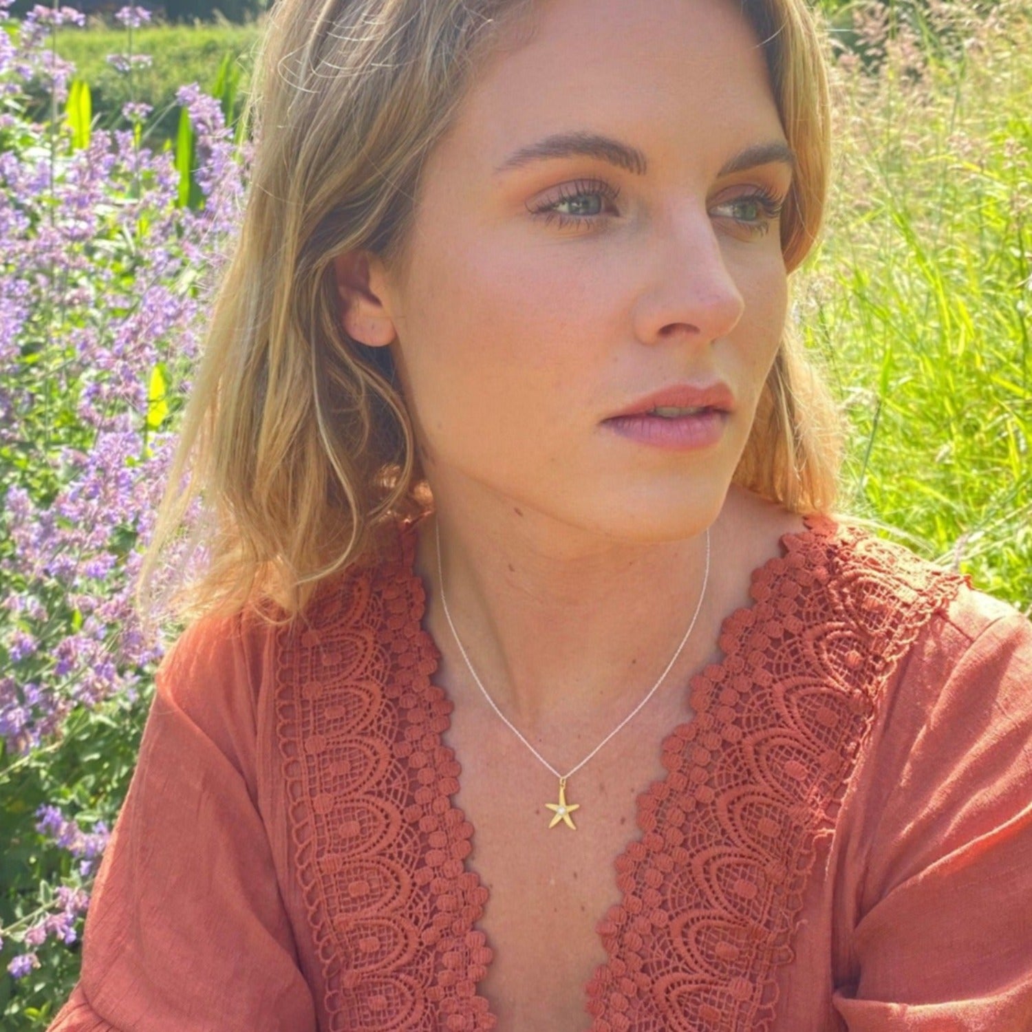 A sterling silver and 18ct gold plate starfish pendant with a white pearl in the centre. worn on an adjustable silver chain on a model.