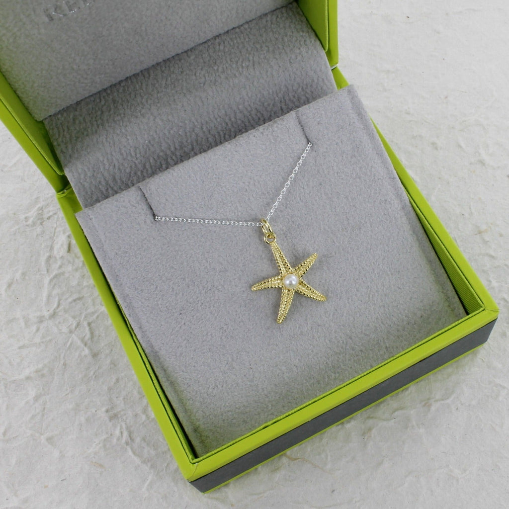 An 18ct gold plate textured starfish pendant with a white pearl at the centre. Hanging on a silver adjustable chain and shown in a Reeves & Reeves branded grey and green gift box.