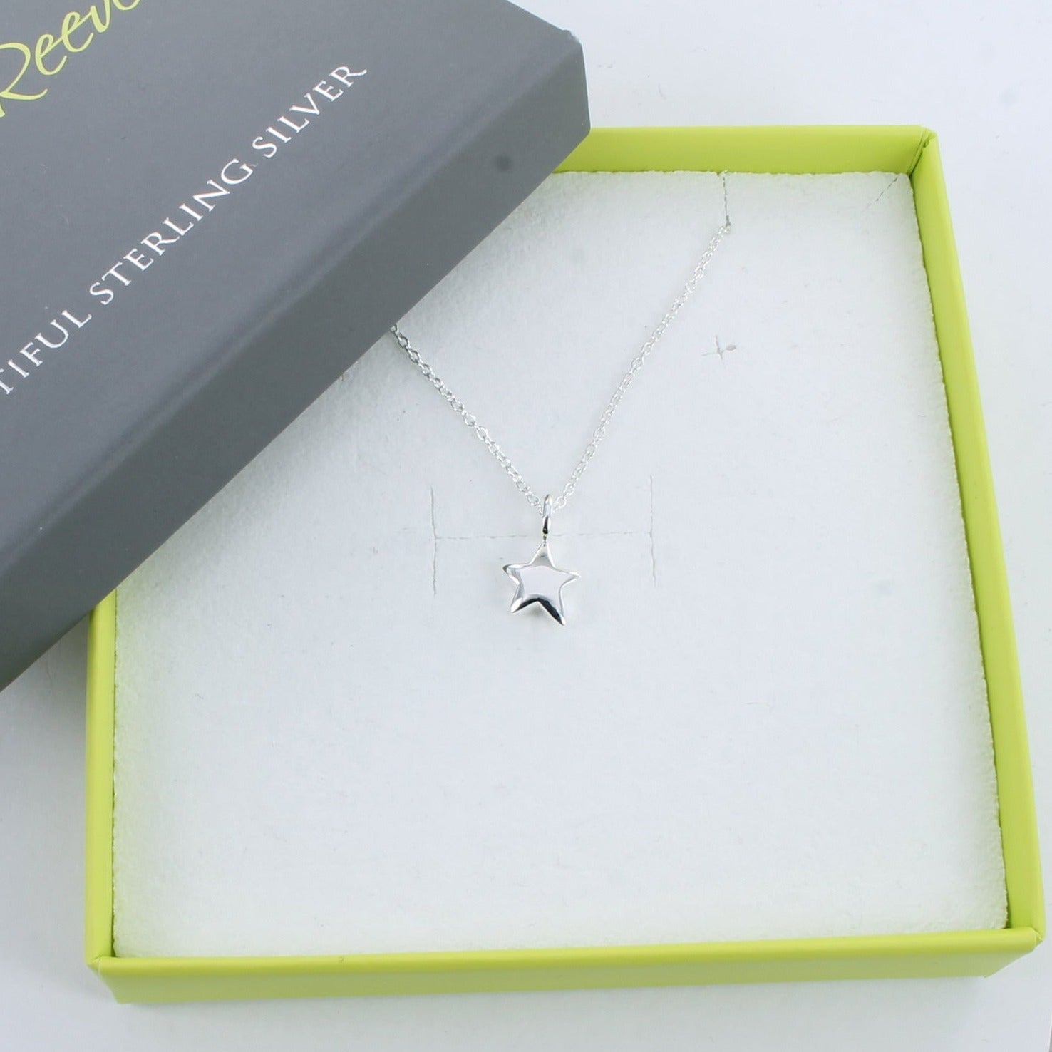 A silver star pendant hung on a silver chain and shown in a Reeves & Reeves grey and green branded gift.