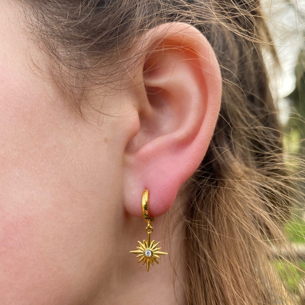 A sterling silver and gold plated hoop earring with a star hanging from the bottom which has a cubic zirconia in the middle and worn in a ladies ear.